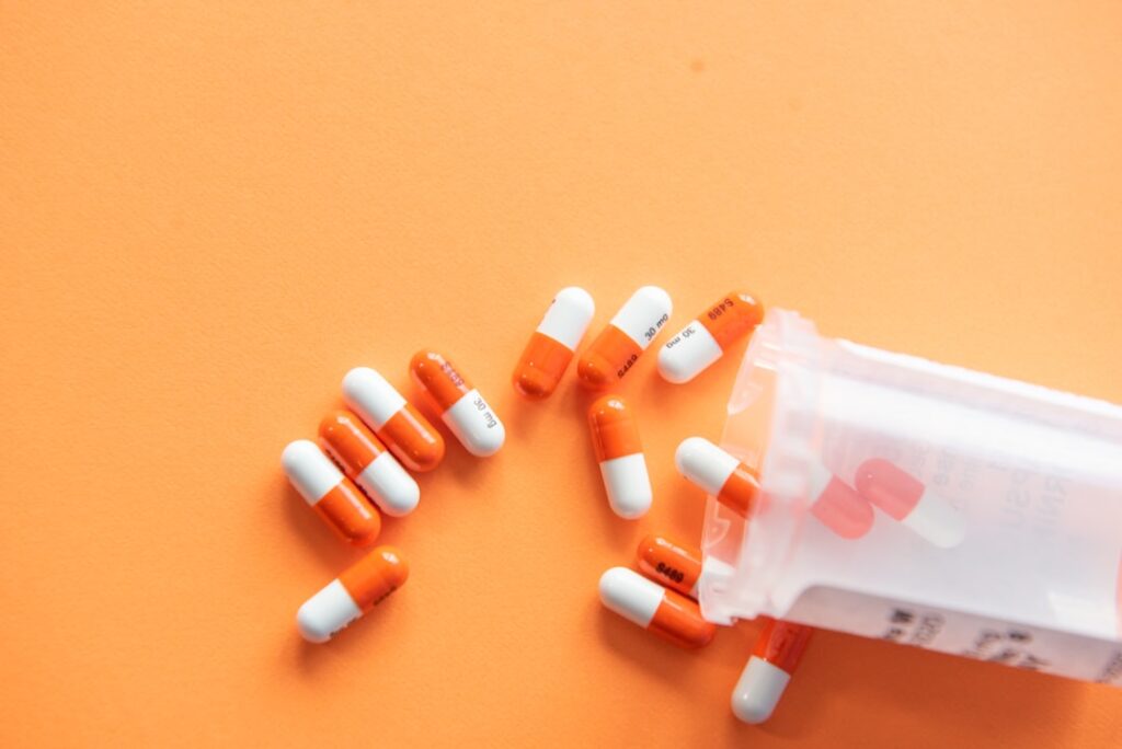 A patient holds a bottle of Augtyro pills while a doctor reviews medical scans on a monitor in a clinic.