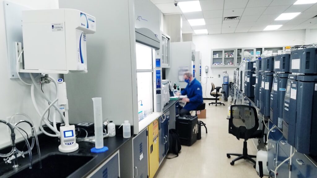 A scientist in a lab coat examines a vial labeled with an experimental cancer drug in a modern laboratory setting.